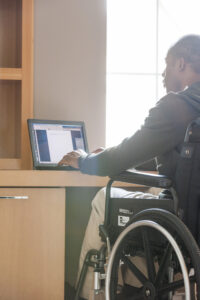 Persona en silla de ruedas usando una laptop sobre un escritorio.