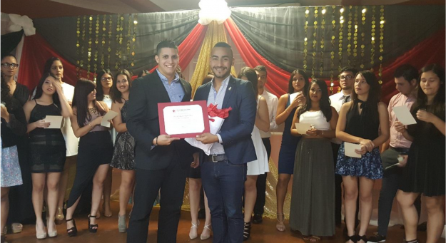 El Sr. Miguel Hernández, Coordinador de Servicios de Voluntarios entrega a Kenneth López, presidente de CRAUPRAg, el certificado que los reconoce como organización estudiantil afiliada a la Cruz Roja Americana