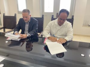 Director de AFI Eduardo Rivera Cruz y el Presidente de la UPR Luis A. Ferrao sentados en una mesa firmando unos papeles.