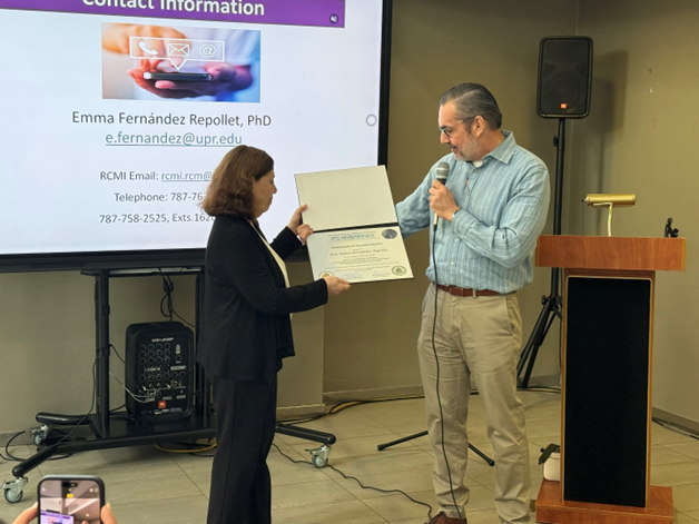 La Dra. Emma Fernández-Repollet recibe un certificado de reconocimiento de parte del personal de la Biblioteca Conrado F. Asenjo.