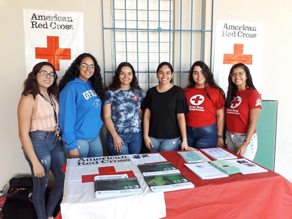 Estudiantes de la U.P.R. en Aguadilla en una mesa. Las estudiantes están como voluntarias repartiendo información sobre la Cruz Roja Americana.