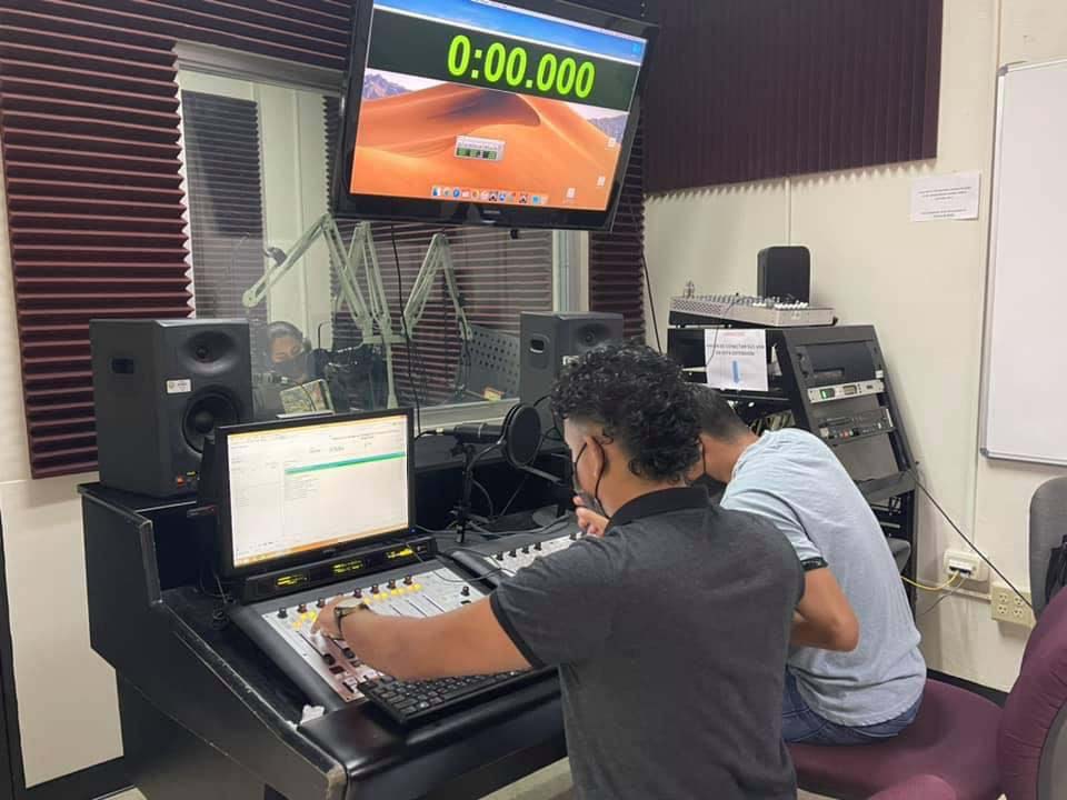 Dos estudiantes operando una consola que controla audio y video en un cuarto a prueba de sonido.