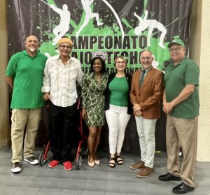 Grupo frente a un afiche que anuncia la Tercera Edición del CAAMpeonato Bajo Techo Wilfredo Maisonave