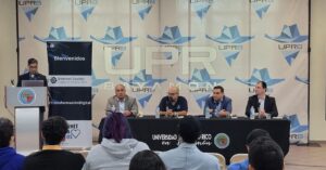 Vista del podio con varios panelistas. En el fondo se ve el logo de la UPR Bayamón.