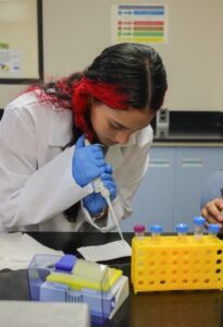 Una estudiante con bata transfiriendo un liquido a un papel de prueba