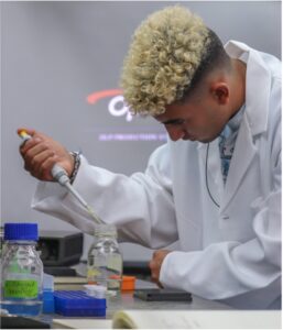 Estudiante con bata, transfiriendo un liquido de una pipeta a otro recipiente de cristal.