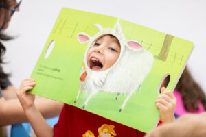 Una cartulina que tiene una cabra dibujada.  Hay un agujero en el espacio que corresponde la cabeza.  Por ese agujero un niño asoma su cabeza sonriendo.