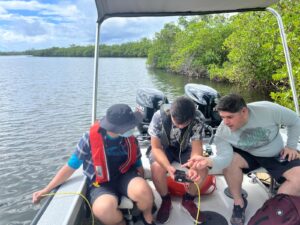 Estudiantes en bote con instrumento en mano.