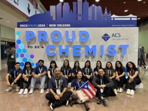 Capítulo Estudiantil de la UPR-Aguadilla sentado frente a un mural que lee 