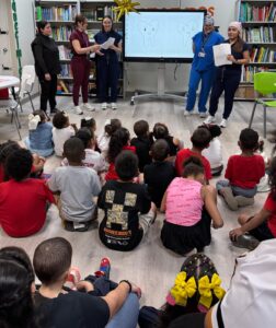 Doctores en un salon frente de niños que están sentados en el piso