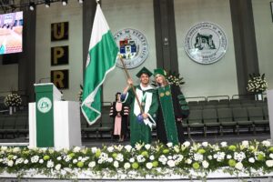 Dos estudiantes en tarima sosteniendo la bandera de la UPR Recinto de Mayagüez