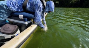 Estudiante con traje impermeable tomando muestras desde un lado del barco.