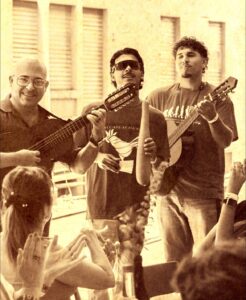 Foto en color sepia, 2 guitarristas y un güirero frente al publico.