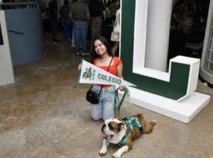Estudiante con banderín del Colegio, arrodillada junto con Tarzán el perro bulldog mascota de la UPR Mayagüez.